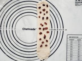 从中间开始分别向上向下擀开成长条形。在面团上铺上蜜豆，收尾处2厘米内不用铺。