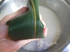 把上面的粽叶像下折盖住米。多余的尾巴折回来。