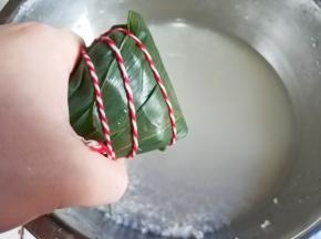 大拇指压住线绳绑住粽子。