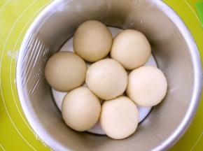 全部包裹好后，将奶酪包放入模具内，如图外圈6个，中间一个的摆放，盖保鲜膜室温发酵至两倍大，因为奶酪馅是冰箱冷冻的，在包裹好后，内馅降低了面团的温度，发酵的时间比较慢，没关系，慢慢等待就行