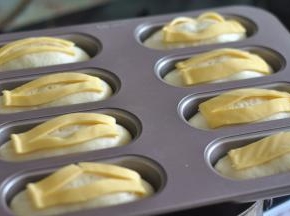 将芝士片切成长方形，盖在面包上，同时芝士片中间也切一刀，往两边一拉，中间形成空白状。