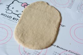 取一份面团擀成椭圆形，稍微用手压一下边缘，尽量排出多余的气体一面做出来的面包组织不够好，一端稍微擀的薄一些。