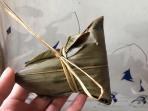 将另一端粽叶压下盖住内馅，按紧，多余的再向一边折起，用石草或绳子紧紧缠绕后绑住