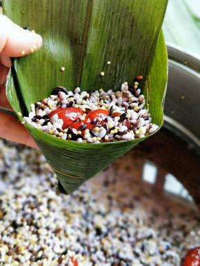 取一片泡好的粽叶，粽叶折成漏洞形，加入杂粮，在加入红枣