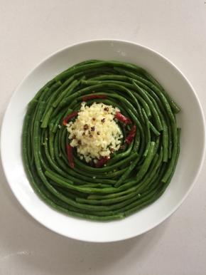 把剁好的蒜末放在豆角的中间位置，摆上干辣椒段和花椒粒。