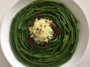 把剁好的蒜末放在豆角的中间位置，摆上干辣椒段和花椒粒。