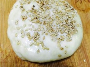 收口朝下，稍微按压成圆饼，表面刷蛋液或者水，表面粘上芝麻，再次轻轻按压，防止芝麻掉落。