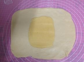 油酥面团放在水油皮面团上压扁，用擀面杖压一压，使它以扁平的状态铺在水油皮中间