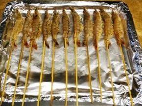 烤盘上放一张锡纸，再刷一点油，以免虾会黏到锡纸上，不用太多有，一层薄薄的油就行，把虾串都放在烤盘上面，把腌制的料也都放在虾上面，这样可以更入味。