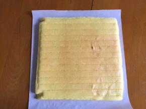 出炉倒扣烤网上，撕掉油纸，蛋糕放至温热，放一张新油纸在上面，翻面