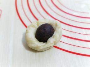 取一块面团压扁包上豆沙馅，收口朝下，揉圆至光滑。依次做完。