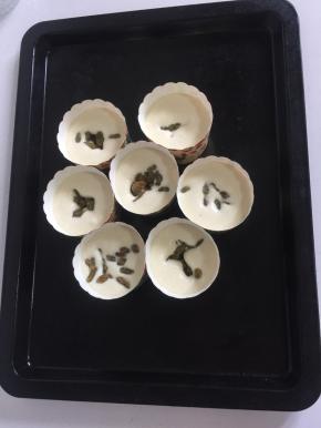 在蛋糊表面撒入适量的葡萄干，把纸杯放进烤盘中。