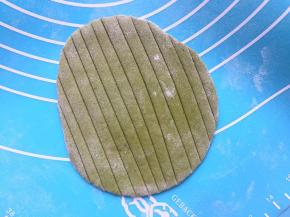 菠菜面团也排气，分割成等量的大小，揉圆盖保鲜膜备用。取一个菠菜面团，擀成稍微椭圆点的片，（圆的、椭圆的包出来的叶子不好看）用刮板压出叶子纹路，在中间剪开