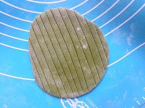 菠菜面团也排气，分割成等量的大小，揉圆盖保鲜膜备用。取一个菠菜面团，擀成稍微椭圆点的片，（圆的、椭圆的包出来的叶子不好看）用刮板压出叶子纹路，在中间剪开