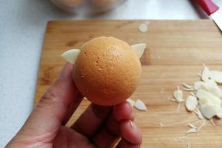 取一个圆球小蛋糕，把修好的杏仁片插在合适的位置当作猫咪的耳朵。