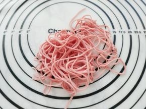将粉色面片压成最细的面条。