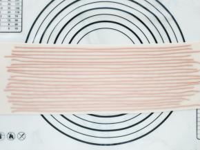 将粉色面条一条一条地铺在白色面片上，再用擀面杖轻轻压一下，使面条粘牢。