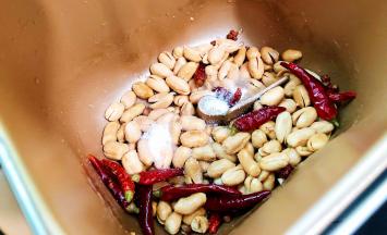 面包机启动炒干果功能，面包机桶内倒入20g的花生油，把花椒，干辣椒冷油放入，加热至搅拌叶搅动就可倒入烤好的花生米，然后就开始调味了，加入盐啦，再加入细砂糖啦