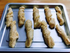 取一块切好的条状面团，双手捏住两头扭几圈，依次做完，放入不粘烤盘中，并间隔距离。