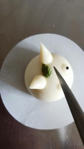 搓一粒黄豆发现的绿色面团成小水滴，抹少许牛奶粘在两个耳朵中间，用刀背压出叶脉