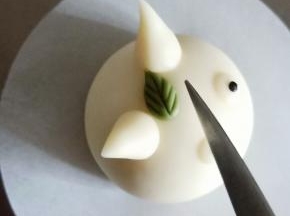 搓一粒黄豆发现的绿色面团成小水滴，抹少许牛奶粘在两个耳朵中间，用刀背压出叶脉