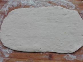 案板上撒适量干粉，发酵好的面团不需要揉面，直接摊放到案析上，用擀面杖将其擀成大长方形面片。