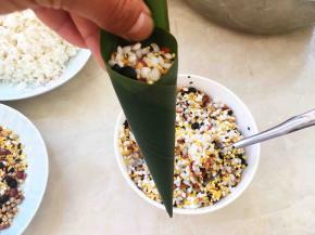 用小勺装入一点拌好的糯米十二谷米，用筷子往底部戳一下，让米进入锥子尖部分，免得煮好的粽子底部是空的，之后再装入米，将锥子筒装满