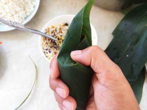 用手指轻轻压下表面，将两侧的粽叶折回来