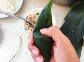 用手指轻轻压下表面，将两侧的粽叶折回来