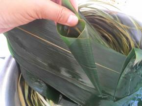 先来做锥形粽子，取一片宽一点的粽叶，卷成细锥形的筒，注意尖部要没有缝隙，免得漏米