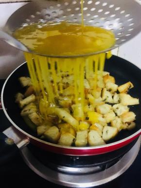 把搅拌好的蛋液通过漏勺，均匀的淋在烤饼丁儿上。