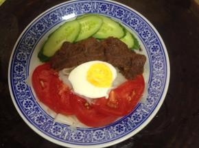 碗底部放入凉皮，上面摆黄瓜、牛肉、番茄和半个煮熟的鸡蛋