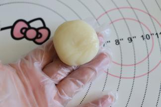 戴好防粘手套，取一个冰皮面团，大约15克，滚圆后，撒适量刚才炒熟的糯米粉，稍微擀开圆形