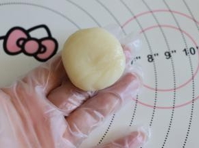 戴好防粘手套，取一个冰皮面团，大约15克，滚圆后，撒适量刚才炒熟的糯米粉，稍微擀开圆形