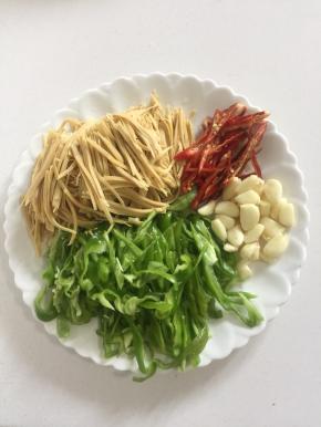 豆干清洗一下切成丝，青椒和红辣椒去蒂切成丝，蒜瓣剥皮拍碎备用。