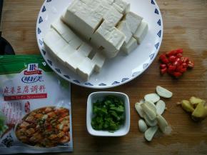 豆腐切小块，在放了盐的沸水中浸泡十分钟。姜、蒜切片。葱切小段，小米椒切丁。