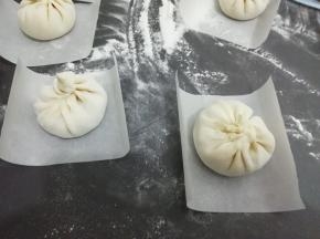 饧好的面团揪成适当的剂子，擀成中间厚，四周薄的圆饼，然后放入适量的馅料包好，底下铺一张油纸