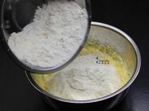 将过筛的面粉、泡打粉，倒入打发好的黄油里，用刮刀稍微拌均。