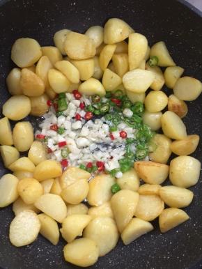 把洋芋拨到两边，放入蒜末，青红尖椒圈儿爆香，再翻炒均匀。