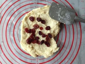 将面团倒在揉面垫上，用刮刀抹平一下面团，倒入1/2的蔓越莓干。折叠后，压平，再放入剩余的蔓越莓干