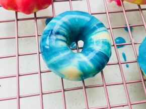 19、	选一个浅色的图片来做示范。如果你想做花纹的，只需要用牙签粘上色素，在白色膏体内搅动几下即可。将甜甜圈正面朝下，放入膏体内。沾均匀膏体后，提起翻面摆于晾架上即可。