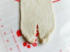 用擀面杖从小头向上擀，擀成一头尖一头宽的形状。
然后翻开过，将宽的一头中间剪开，向上卷起，再由上向下卷起，收口处压在下面，捏紧。