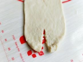 用擀面杖从小头向上擀，擀成一头尖一头宽的形状。
然后翻开过，将宽的一头中间剪开，向上卷起，再由上向下卷起，收口处压在下面，捏紧。