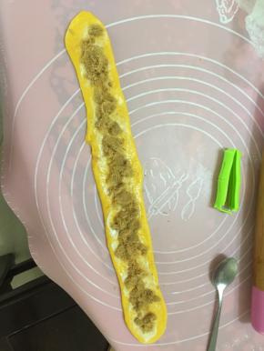用擀面杖将面团擀成长舌状，刷上沙拉酱，放入肉松，将面团由上而下地卷起