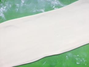 取出发酵好的面团，在揉面垫上撒上少许干粉，用手揉搓面团排气，并将面团再次揉成光滑的状态，接着将面团一分为二，将面团用擀面棍擀长擀宽。