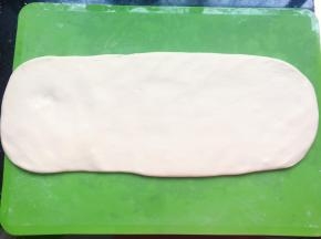 在硅胶垫上撒上少许面粉，将醒发好的面团擀开，擀的时候边抻边擀，不用擀太宽，尽量抻长一点。