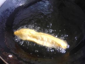 再捏住面胚的两头，捏紧一点，否则炸的时候容易散开，将面胚拉长一点，放入烧至六成热的油锅里油炸。炸的时候要用筷子不停地翻动，这样才能受热均匀。