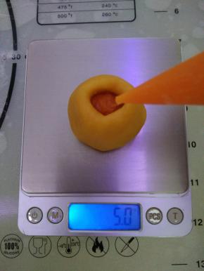 将所有馅料一起抠好备用，记得要盖好保鲜膜。取一个馅料放在厨房秤上，注入流心馅。一只手拿起馅料，别一只从流心馅最高的位置用手慢慢边排气边收口。