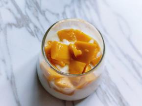 首先取一个杯子，将酸奶倒入杯中，再将切好的芒果加入。