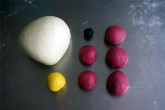 将发酵好的面团按压排气后分别揉圆，然后将红色面团分成2份20克的，3份30克的小面团，揉圆。用保鲜膜将面团盖好。